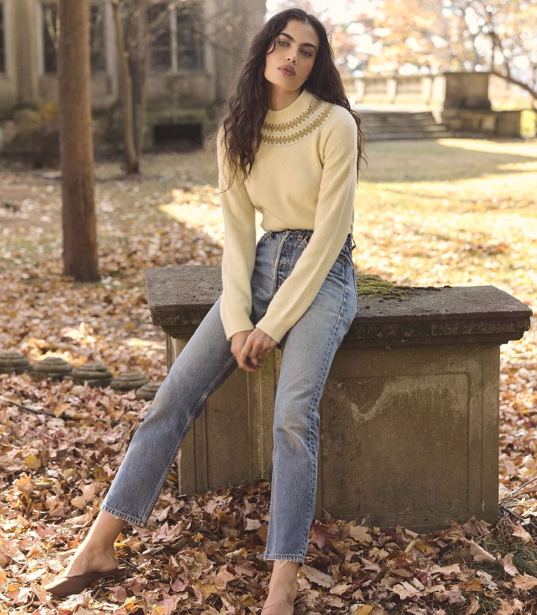 Woman wearing stylish knitwear in a fall setting surrounded by autumn leaves.